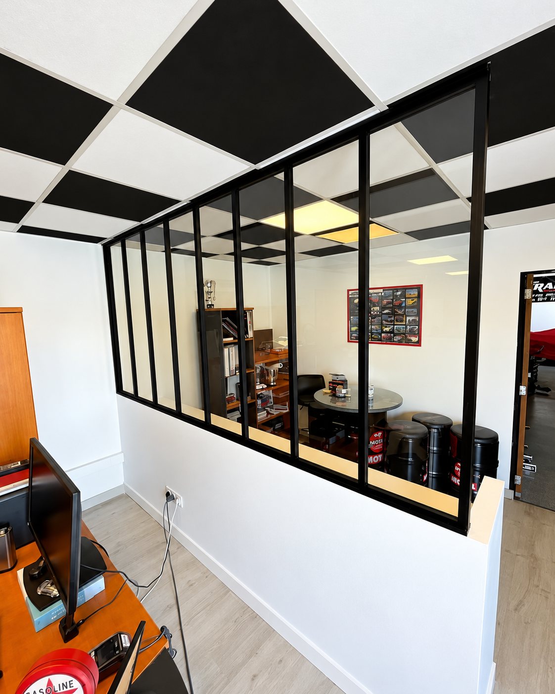Intérieur d'un bureau séparé d'une salle de réunion par une verrière d'atelier noire, avec un plafond à dalles noires et blanches.