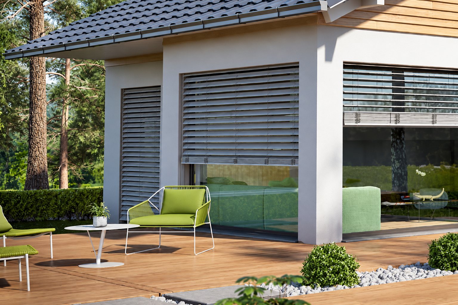 Une terrasse en bois devant une maison moderne dont les grandes baies vitrées sont équipées de volets à lames orientables, avec des fauteuils verts et une table basse blanche.