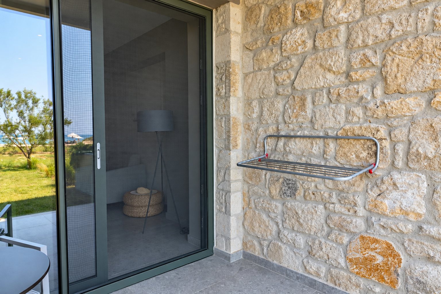 Une porte coulissante vitrée à moustiquaire donne sur une terrasse, avec un étendoir métallique fixé à un mur en pierre naturelle.